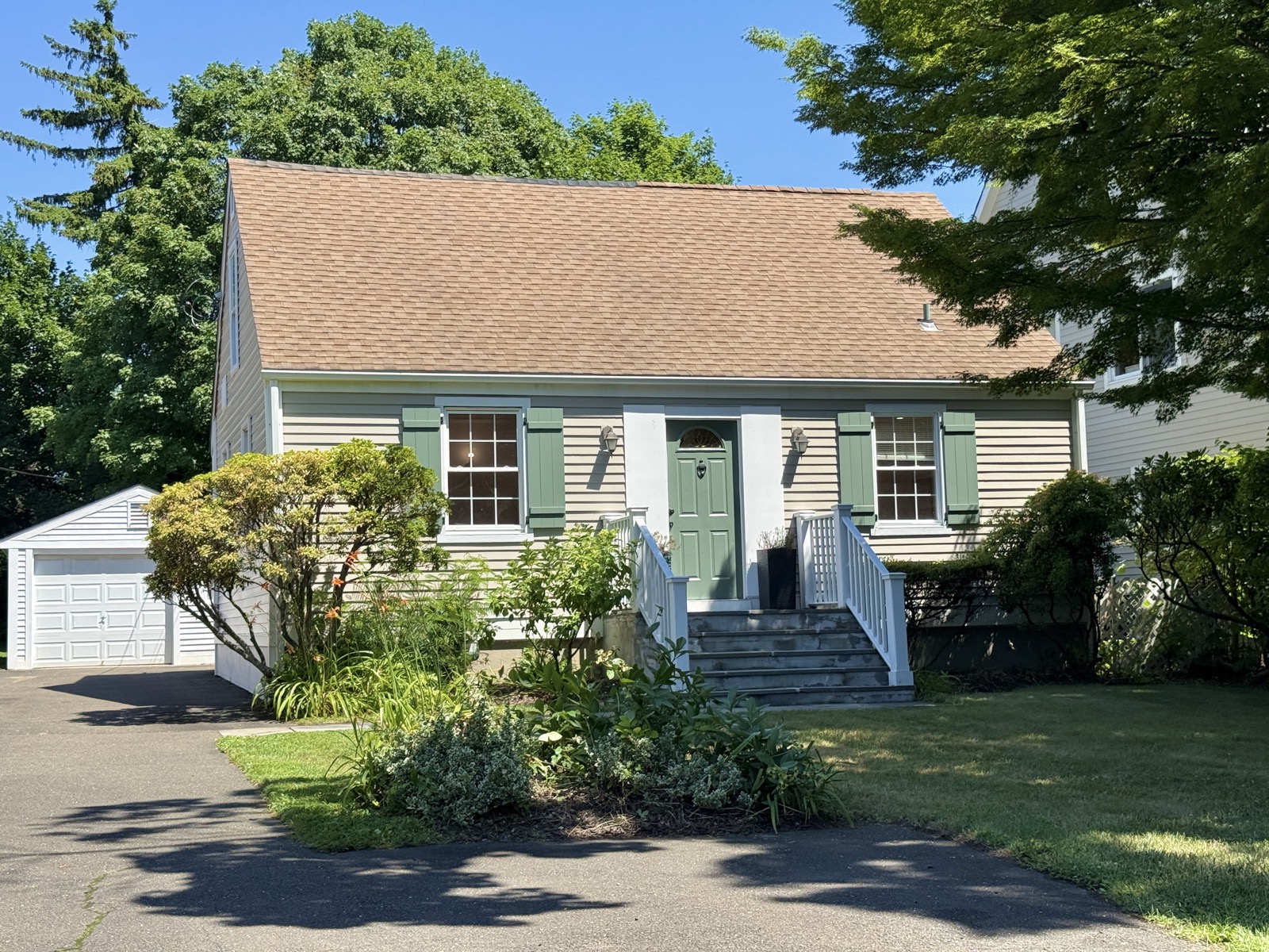 Classic Cape-style home with green shutters and a front garden on a sunny Stamford, CT street
