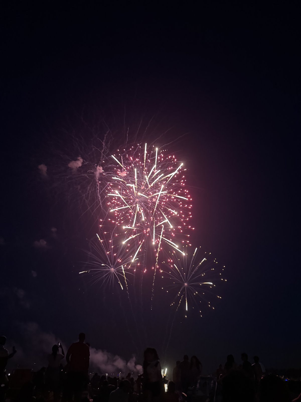 Multiple fireworks bursts in red and gold over a summer crowd in Stamford, CT